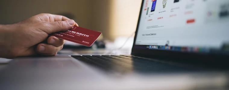 A card held out to a shopping site open on a laptop